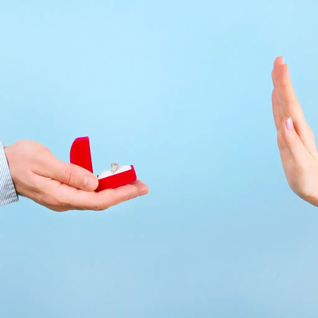 A man proposing to a woman with an engagement ring in a red velvet box. The woman is holding up her hand as a refusal 